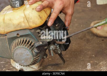 Close up hands using screwdriver to repair small combustion engine motor outdoors focusing with concentration fixing broken equipment detail part mech Stock Photo