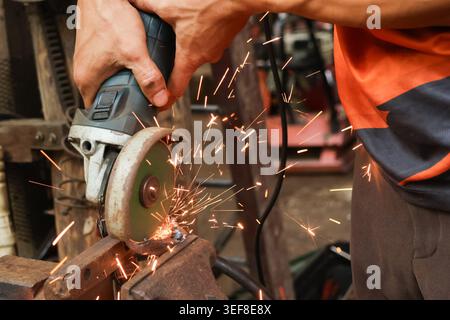 Close up worker hand using electric angle grinder cutting metal with bright flying orange spark in industrial workshop showing intense focus on manufa Stock Photo