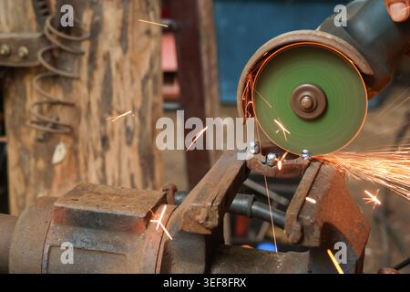 Focused worker operating an industrial angle grinder tool cutting heavy metal piece creating bright hot spark intense manual labor dedicated manufactu Stock Photo