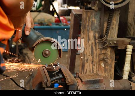 Focused worker operating power grinder cutting heavy metal inside workshop creating bright spark flying from tool during intense manual labor and meta Stock Photo