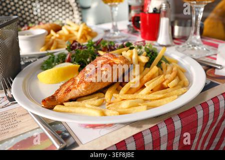 Grilled salmon fillet plate served with crispy french fries and fresh green salad. Golden fish steak features juicy texture accompanied by lemon wedge Stock Photo