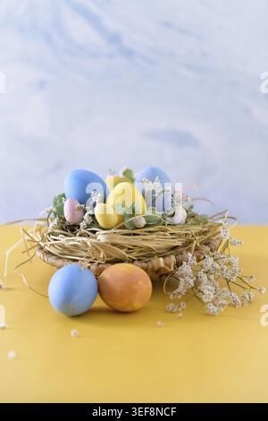 Easter eggs in nest on blue background and yellow table Stock Photo