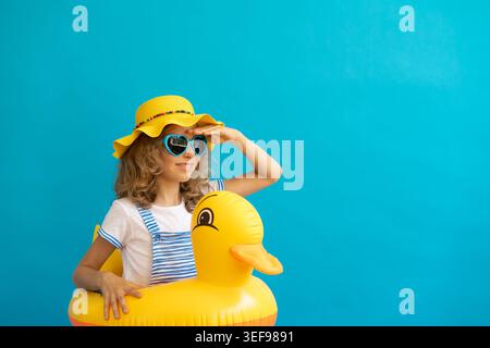 Portrait of happy child with yellow rubber duck against blue background. Girl having fun on summer vacation. Dream and imagination concept Stock Photo