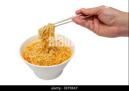 hand holding chopsticks with korean instant noodles in white bowl isolated on white background Stock Photo