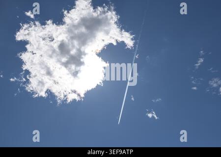 An airplane contrail next to a large cloud in the blue sky, Ternitz, Lower Austria, Austria Stock Photo