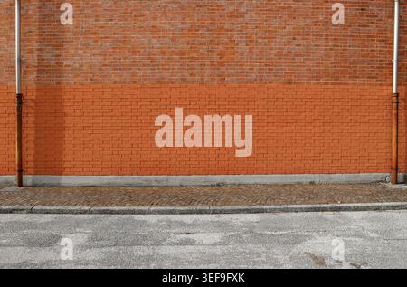 Bicolor brick wall with two gutters at the ends. Porphyry sidewalk and paved road in front. Background for copy space. Stock Photo