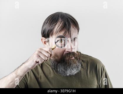 Bearded man looking through magnifying glass. Surprised Male detective Stock Photo