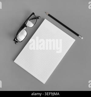 Blank copybook, pencil and glasses on gray paper background. Responsive design mockup. Top view. Flat lay Stock Photo