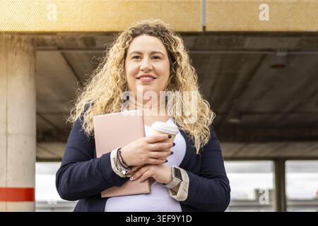 Portrait of smiling female entrepreneur in formal suit with tablet and coffee outdoors. Young smart casual clothing businesswoman portrait Stock Photo