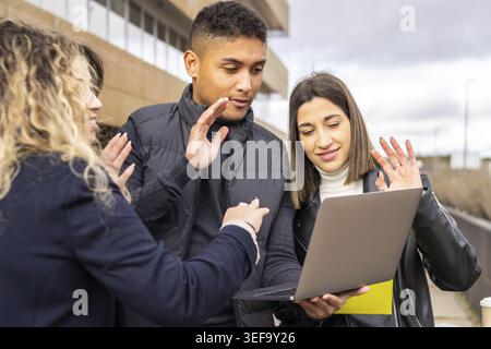 Portrait of a group of multi-ethnic young entrepreneurs waving at the computer conducting a video conference in the street. online business meeting Stock Photo