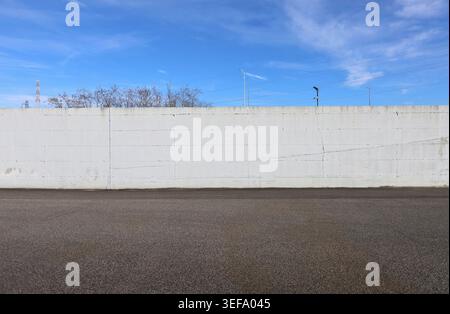 White concrete boundary wall with blue cloudy sky, trees, street lights and transmission towers on behind . Street in front. Background for copy space Stock Photo