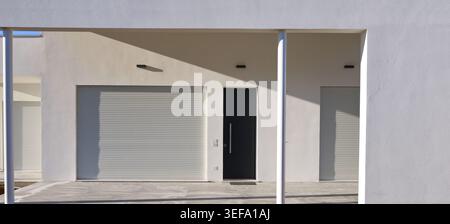 Modern house porch entrance with white palster wall and large roller shutters closed. Side light, background and texture. Stock Photo