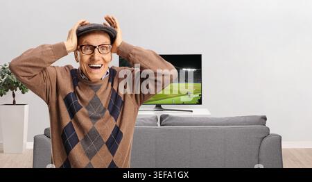 Surprised elderly man holding his head and watching a football match on tv Stock Photo