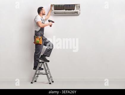 Worker on a ladder repairing an indoor AC unit Stock Photo