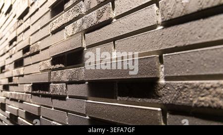 A low-angle perspective shot of a dark layered brick wall with metallic inlay accents reveals intricate masonry detail and strong horizontal lines receding into the distance. Rich texture and depth make this ideal as an architectural design background. Stock Photo