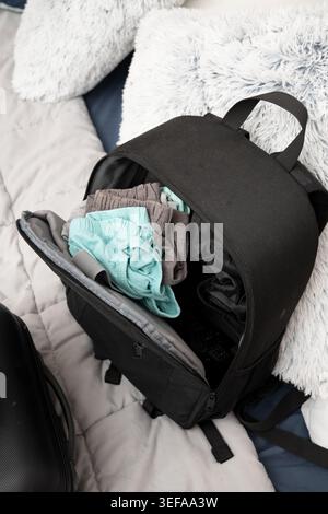 Black backpack opening on bed, packing clothes for travel Stock Photo