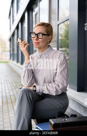 Sophisticated adult woman engages in a pleasant phone conversation while sitting outside. Stock Photo