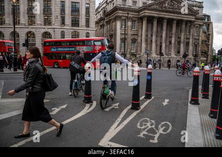 A cyclist straddles two City of London bollards to keep balance whilst waiting for traffic lights to turn to green at Bank junction in the Square Mile. Stock Photo