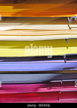 Stacks of colorful felt fabric sheets, paper in orange, red, green, brown, and blue on a metal shelf. Craft materials displayed in a store, ideal for Stock Photo