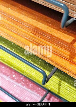 Stacks of colorful felt fabric sheets, paper in orange, red, green, brown, and blue on a metal shelf. Craft materials displayed in a store, ideal for Stock Photo