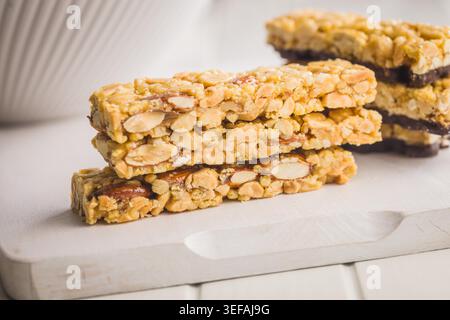 Stacked crunchy peanut brittle nut bars with visible almonds and caramelized glaze presented on a wooden board, evoking homemade snack time, sweet indulgence and crunchy texture for dessert or treat. Stock Photo