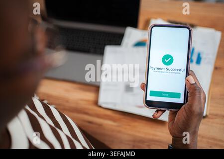 Person holding smartphone displaying successful payment notification, confirming a completed transaction Stock Photo