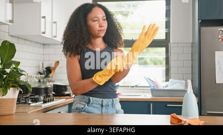 Woman Putting On Yellow Cleaning Gloves in Modern Kitchen Preparing to Clean Counter Stock Photo