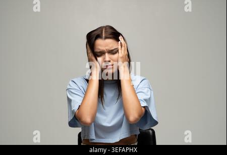 Young woman feeling intense head pain, suffering from migraine, stress, and anxiety, pressing her hands to her temples Stock Photo