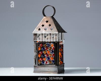 Decorative wrought iron metal lantern with colorful red blue orange glass marbles in lattice and star shaped cutout roof on plain grey backdrop studio Stock Photo
