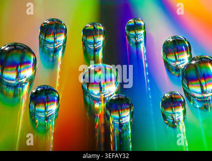 Iridescent water droplets glide across a rainbow spectrum, creating a vibrant abstract dance of light, motion and reflection. Stock Photo