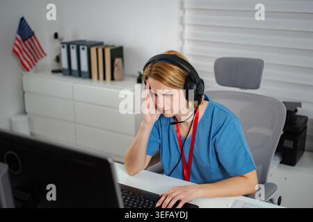 Stressed medical professional working on computer with headset Stock Photo