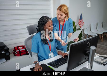 Two nurses collaborating on computer and paperwork at medical office Stock Photo