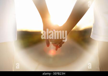 Lovers walking hand in hand along a sunset path, companionship with a loved one, background of a married couple and friends Stock Photo
