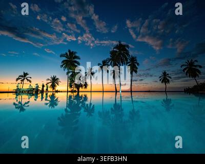 Infinity pool reflects sunset and trees at private resort in Madagascar while guests relax Stock Photo