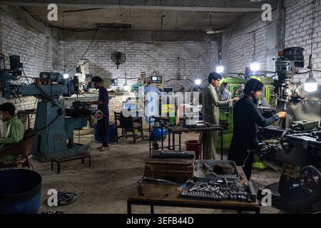 Men work in a gun factory in Peshawar producing firearms and using machinery in a workshop setting Stock Photo