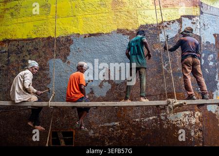 Men repair a boat in a shipwreck yard in Dhaka, Bangladesh while working together on a project Stock Photo