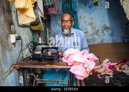 Tailor working at his sewing machine in the Puthia Rajbari Complex with colorful fabrics around him in Bangladesh Stock Photo