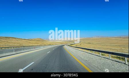 Long and winding road stretches through arid landscape in Northern Azerbaijan under clear blue sky Stock Photo