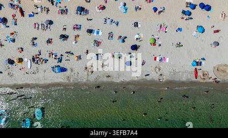 Crowds enjoy a sunny day at Legenese cove beach in Carnac, Brittany, France with umbrellas and activities on the sand Stock Photo