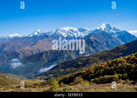 Mountain scenery in North Ossetia with snow-capped peaks and colorful autumn trees under clear blue sky Stock Photo