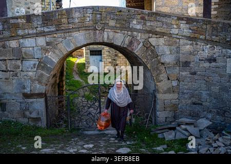 Woman walks under a small bridge carrying a bag in a traditional dress in a village in Dagestan, Russia Stock Photo