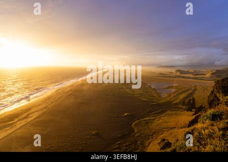 Golden sunset over Dyrholaey coastline with waves breaking on black sand beach Stock Photo