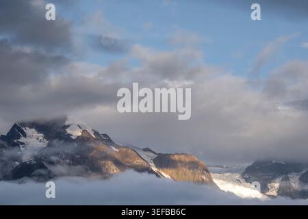 Sunlight breaks through clouds over Meili Mountains in Yunnan during early morning hours highlighting snow and rock Stock Photo
