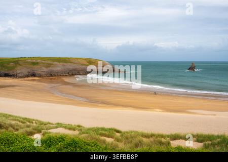 Couple walks with dog past Church Rock on Broad Haven South beach in Pembrokeshire Stock Photo