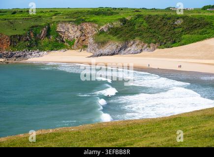 People walking along Broad Haven South Beach as waves crash on the sandy shore in Pembrokeshire, Wales Stock Photo