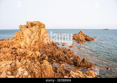 Golden light shines on coastal rocks at Lions Rock in Guernsey during sunset over the Atlantic Ocean Stock Photo