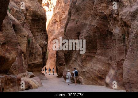 Exploration of a narrow gorge leading to ancient ruins in Petra, Jordan with tourists walking through the landscape Stock Photo