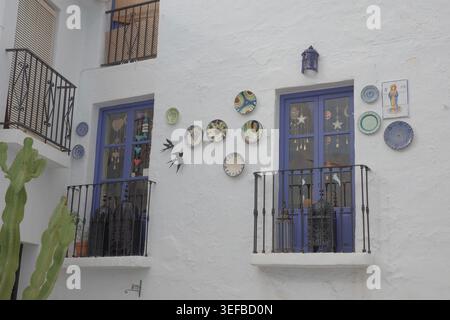 Hand-painted ceramic plates and swallow silhouettes decorating a whitewashed facade with blue-framed balconies in Frigiliana, Andalusia, Spain. Stock Photo