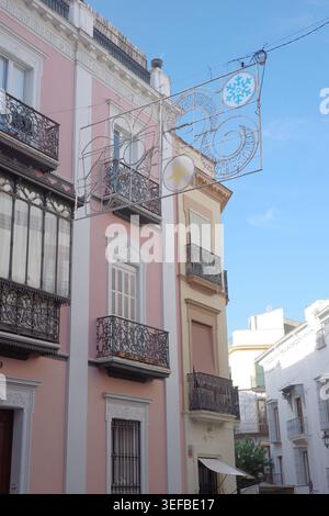 Christmas decorations with snowflake and star motifs suspended above a narrow street lined with pink buildings and iron balconies in Seville, Spain. Stock Photo