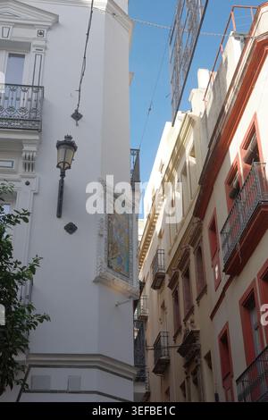 Ornate ceramic tile mural in a decorative plaster frame on a whitewashed corner building with a street lamp in a narrow alley in Seville, Andalusia Stock Photo